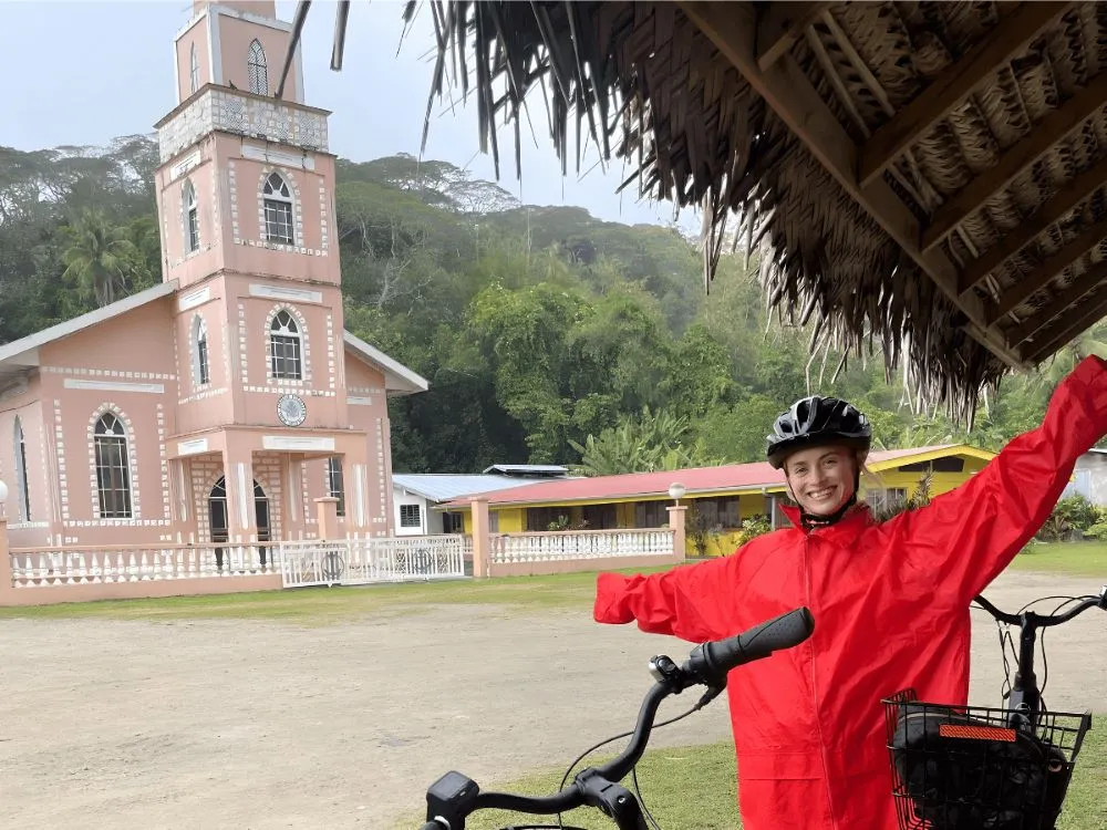Sara in front of a rosa church, cycling around Taha'a in French Polynesia