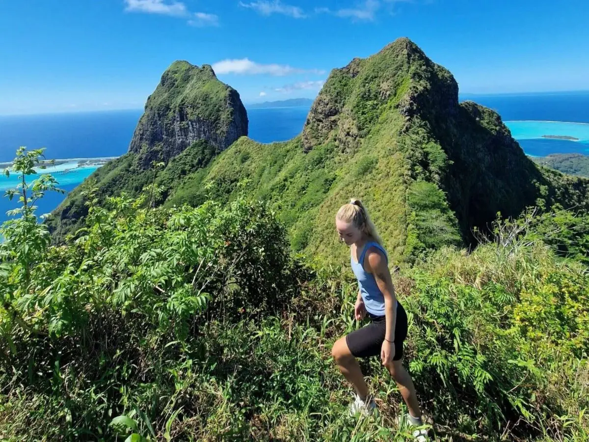 A hiker at the summit of Mount Pahia in Bora Bora, French Polynesia with Mount Otemanu in the background