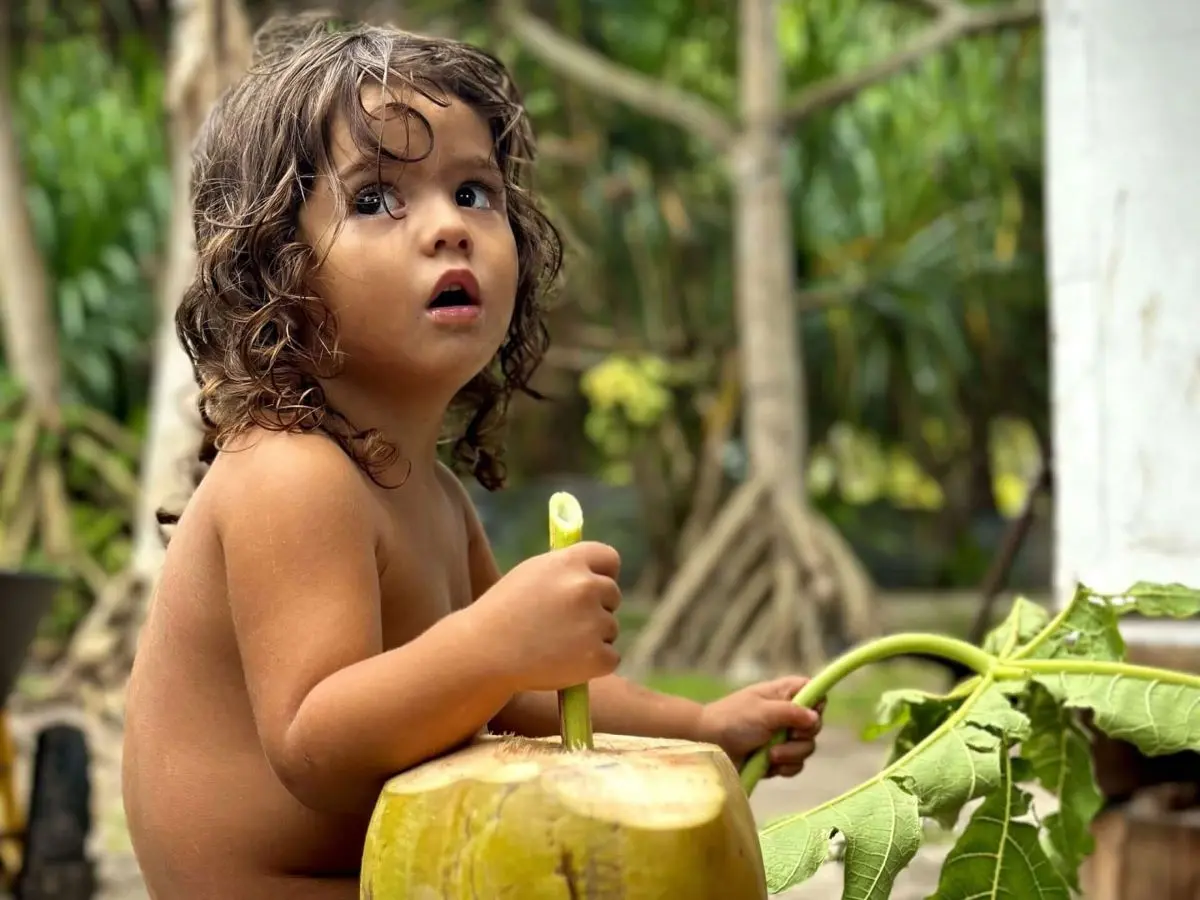 Mica's daughter is drinking coconut water straight from a coconut at her home on a motu in Bora Bora