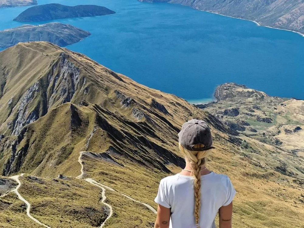 A hiker standing at the summit of Roys Peak Track in Wanaka, New Zealand
